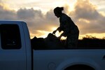 An airman stows luggage in a truck at twilight.