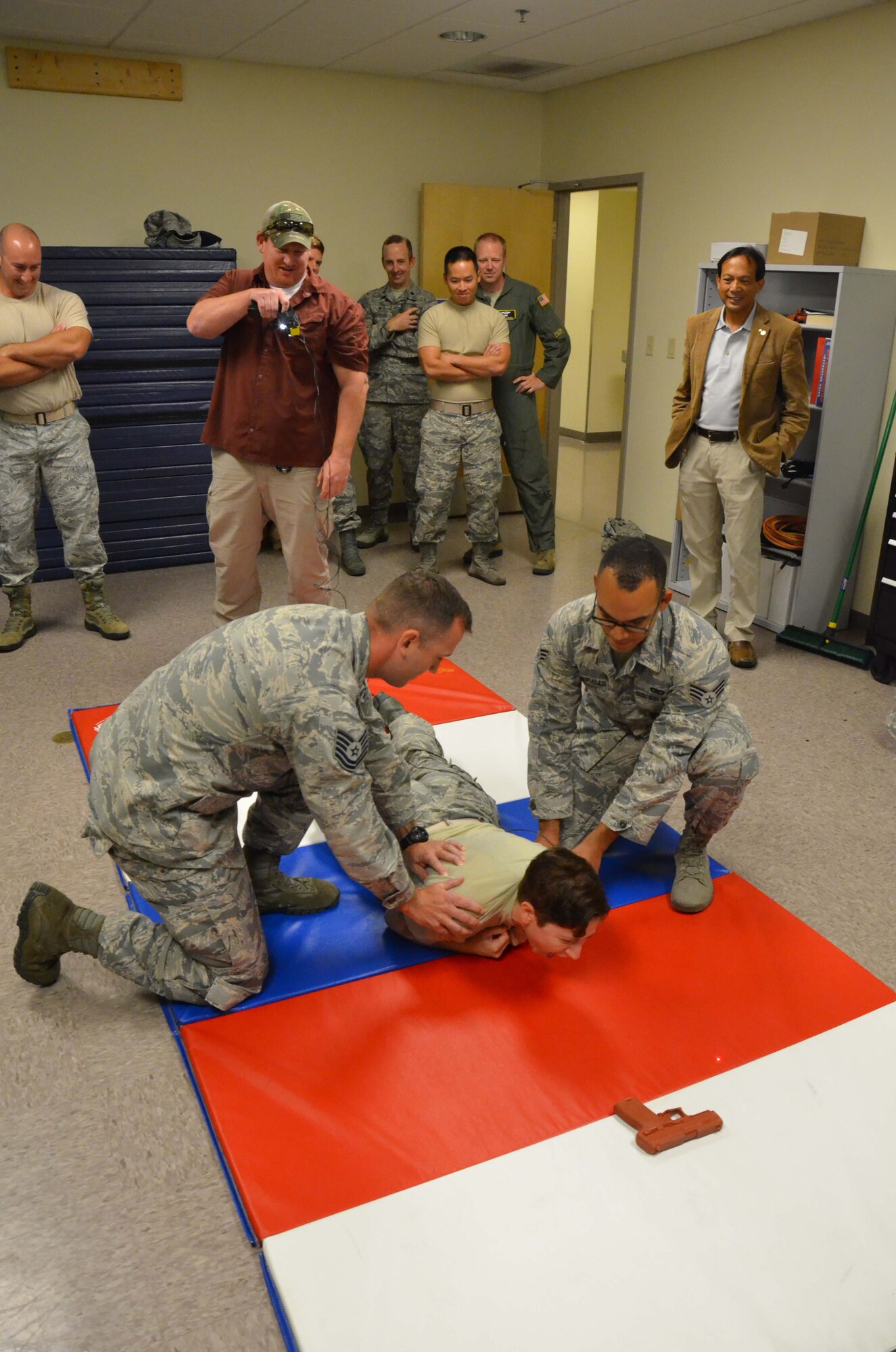 Senior Airman Jenna Bruzual, a spectral analyst with the 21st Surveillance Squadron at Patrick AFB, Fla., is spotted by Tech. Sgt. Thomas Angelini, 45th Security Forces Squadron noncommissioned officer in charge of training, and Senior Airman Steven Morales, 45th SFS unit schedule and training specialist, as trainer James “Chewy” Chenoweth delivers a high voltage jolt with a Taser.  Bruzual was one of 18 Airmen from the Air Force Technical Applications Center who visited the base law enforcement squadron to learn more about their role in personnel and installation protection.  (U.S. Air Force photo by Susan A. Romano)