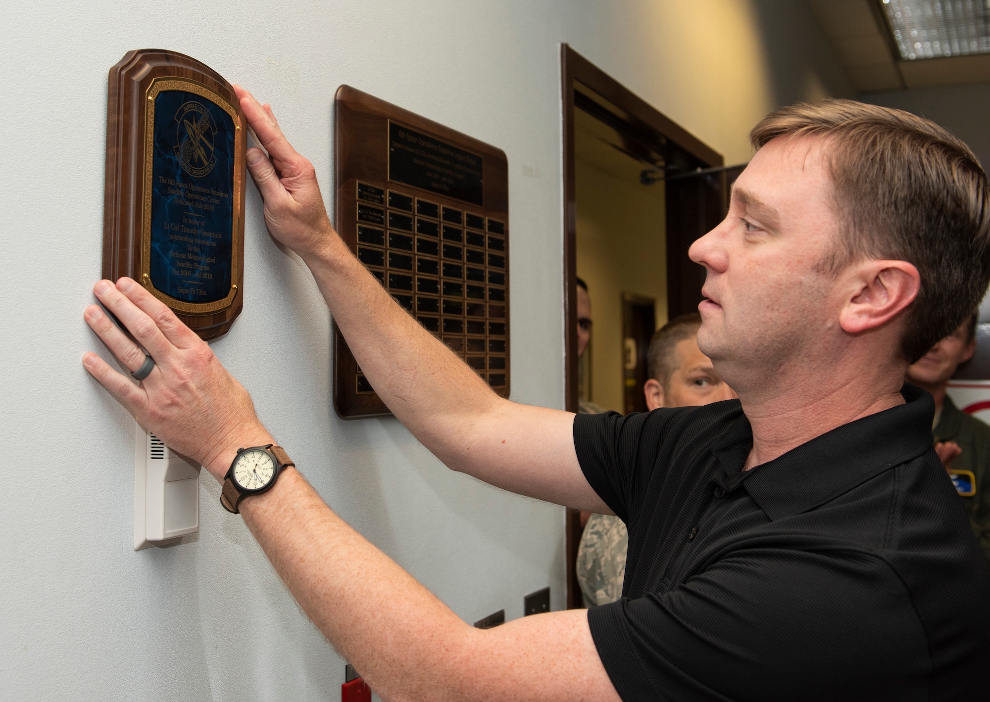 Lt. Col. Timothy Gasmire (retired) hangs a plaque on the wall of the updated 6th Space Operations Squadron operations floor Aug. 4th, 2018.