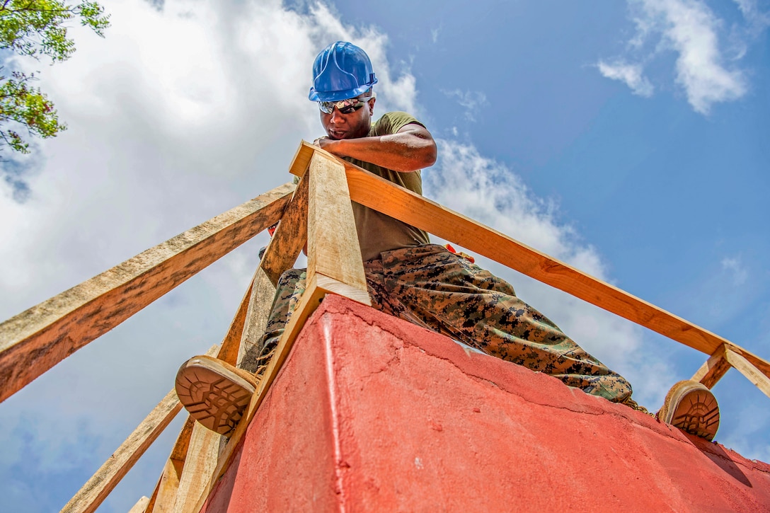 A Marine joins pieces of lumber together for the roof of a building.
