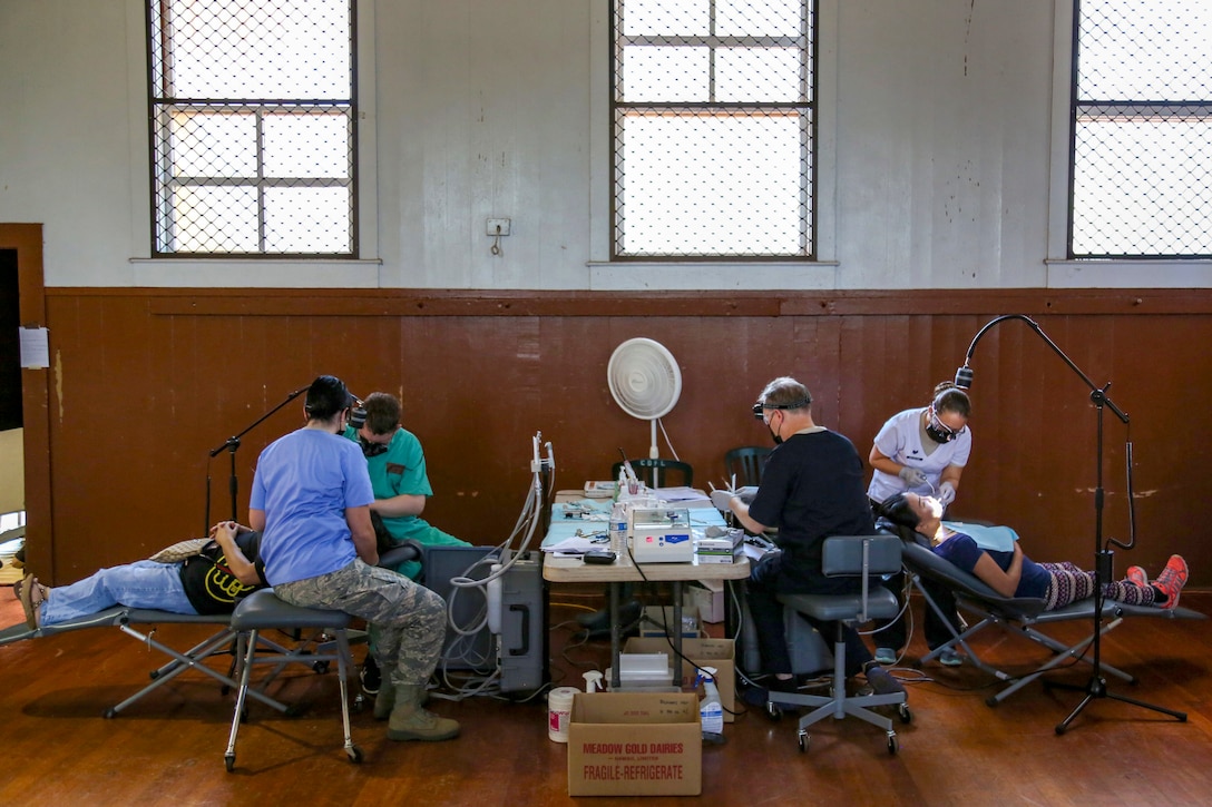 Service members provide dental care to patients in a big room.
