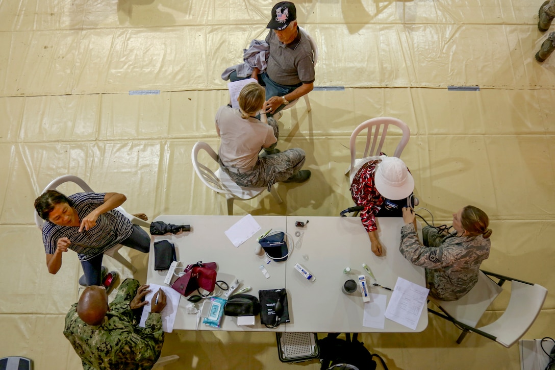 Service members, shown from overhead, take vital signs from patients around a table.
