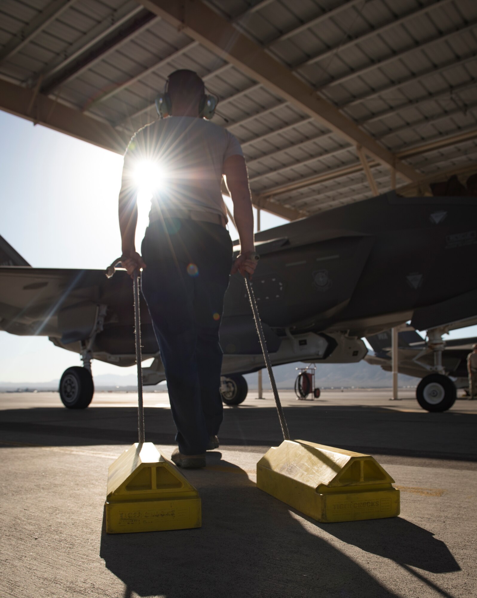 Senior Airman Dustin Hilton, 57th Aircraft Maintenance Squadron Lightning Aircraft Maintenance Unit crew chief, drags a set of chocks to an F-35A Lightning II fighter jet at Nellis Air Force Base, Nevada, July 23, 2018. Placing chocks under the tires of an aircraft prevents it from moving until the pilot is ready to taxi the aircraft to the runway. (U.S. Air Force photo by Airman 1st Class Andrew D. Sarver)