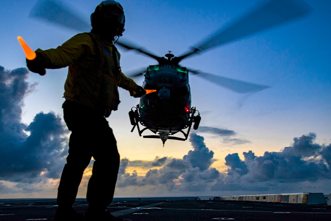 A sailor signals to a helicopter.