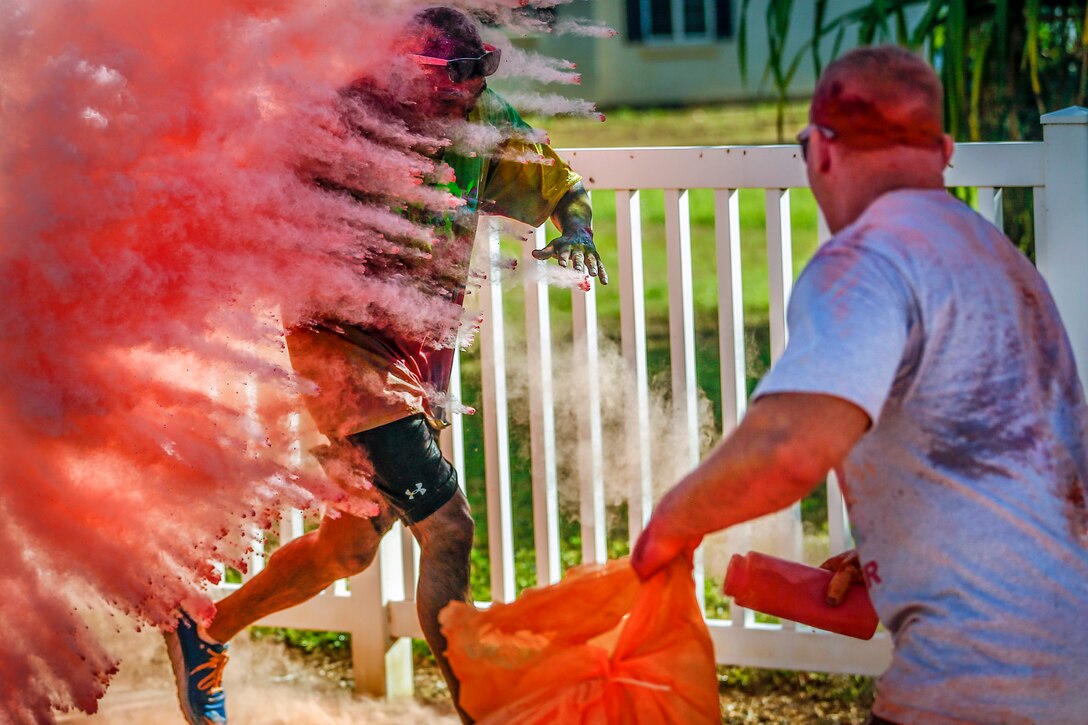 A Marine runs behind a cloud of colorful powder.