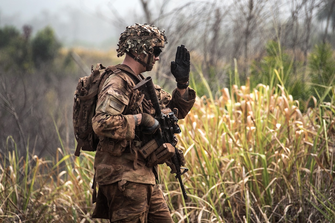 A soldier signals his team to initiate a file formation during a combined arms live-fire exercise.