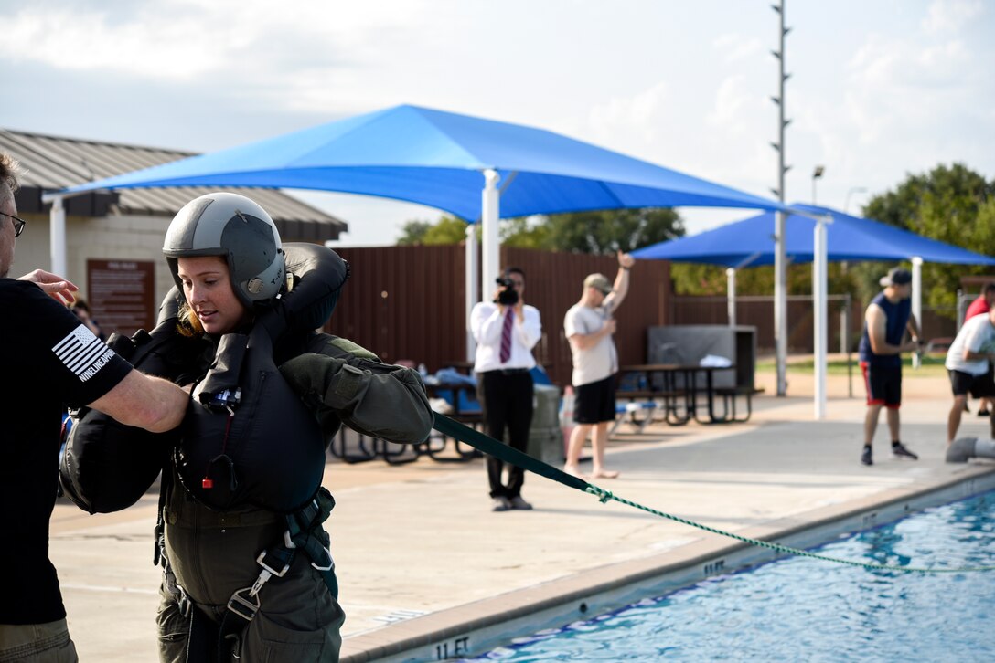 An airman is helped with putting her gear on, before she is pulled by a rope and drug through a pool as part of a training exercise.
