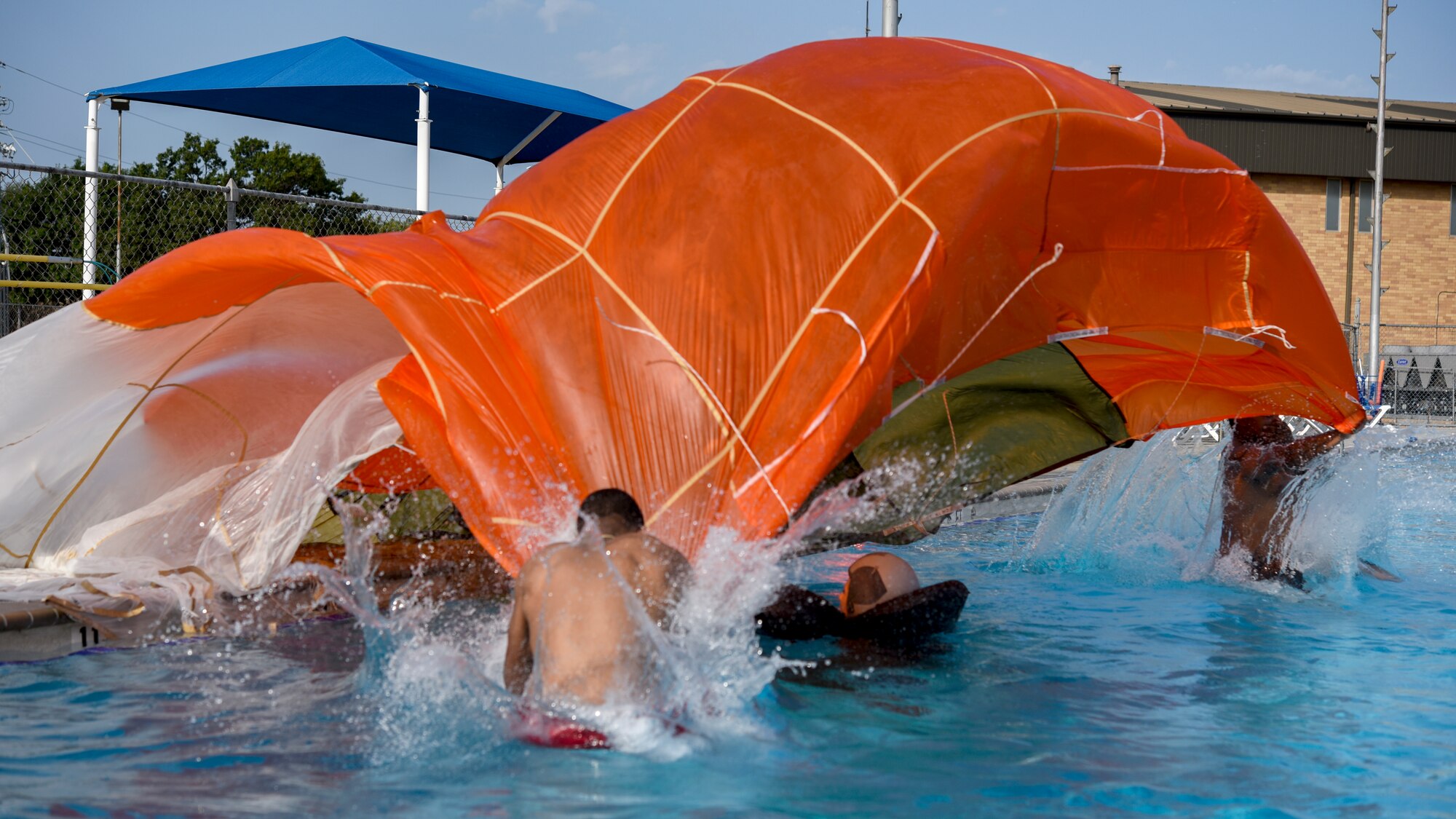 Two airman jump over a swimming pilot as they drape a parachute over her as part of the second scenario in the Water Survival Emergency Training.