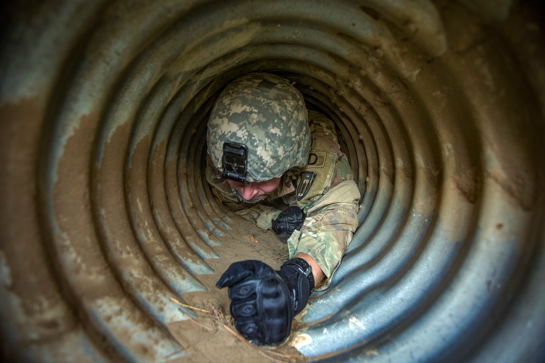 A soldier pulls himself through a narrow tunnel.