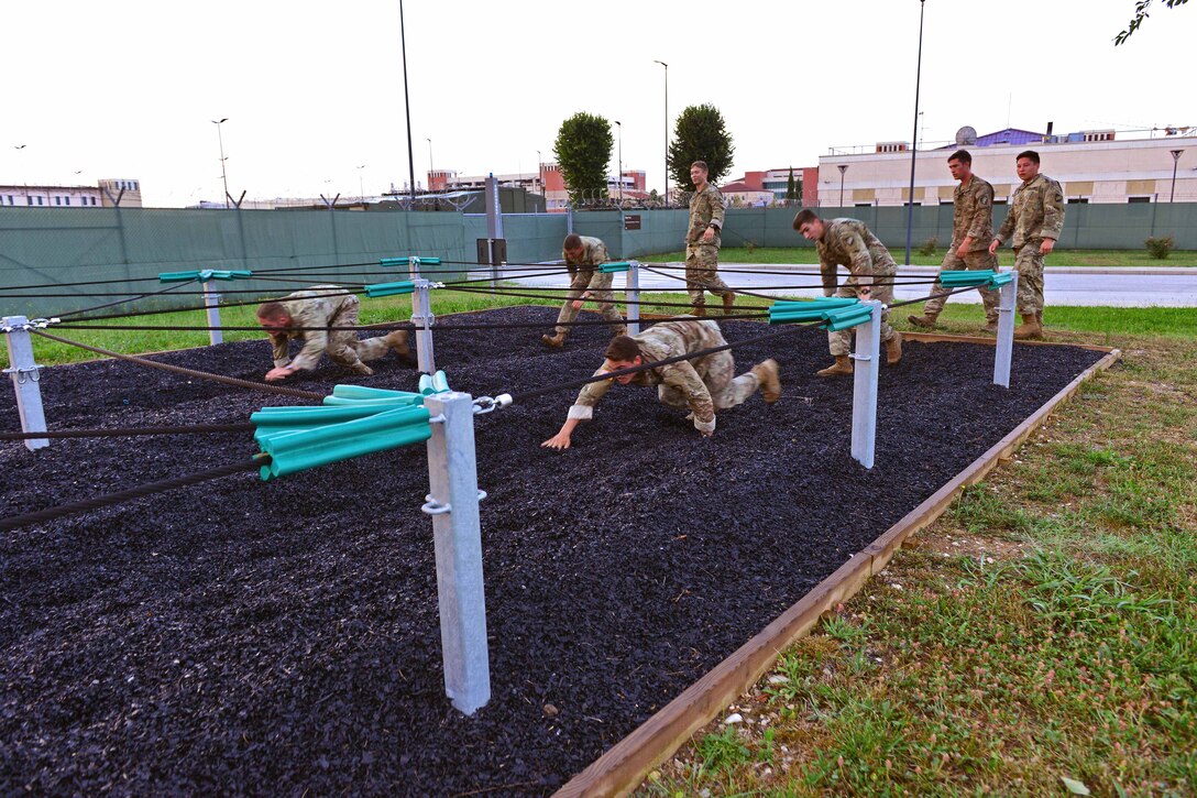 Soldiers low-crawl under rope during the obstacle course.