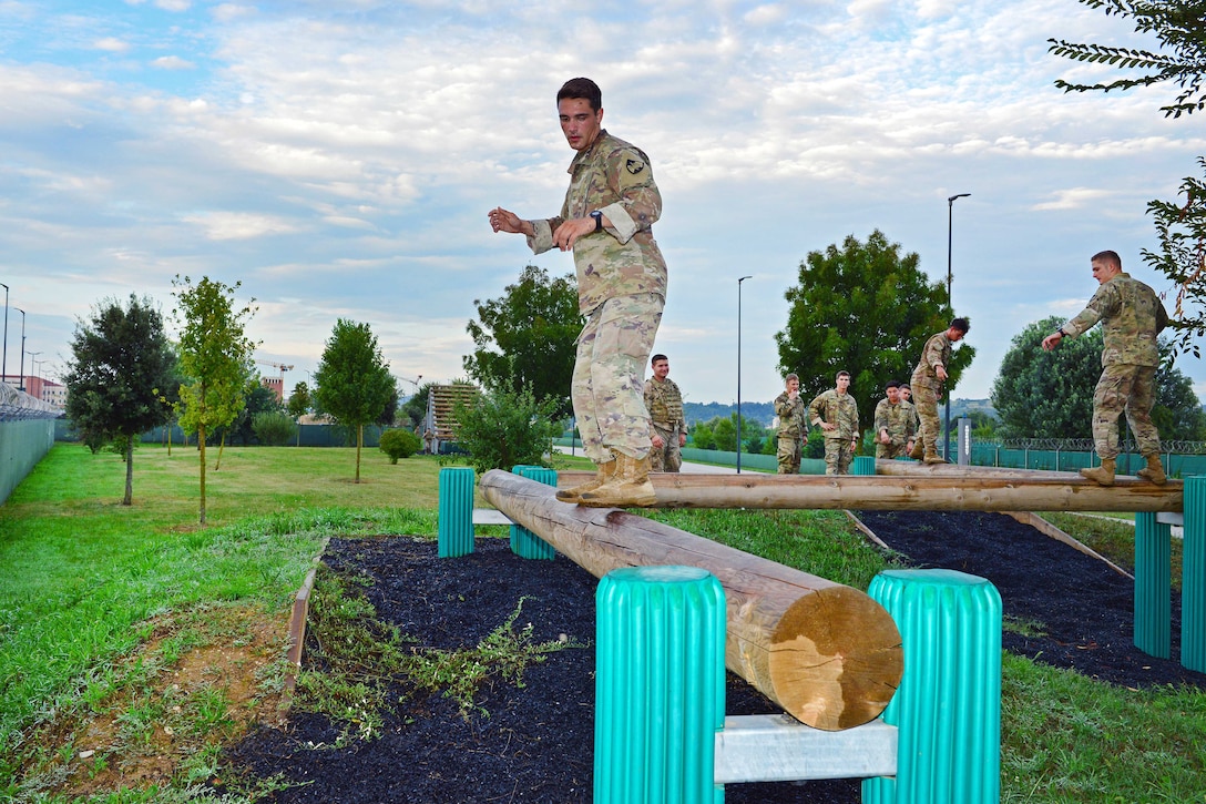 Soldiers balance on logs while maneuvering along the balance beam obstacle course.