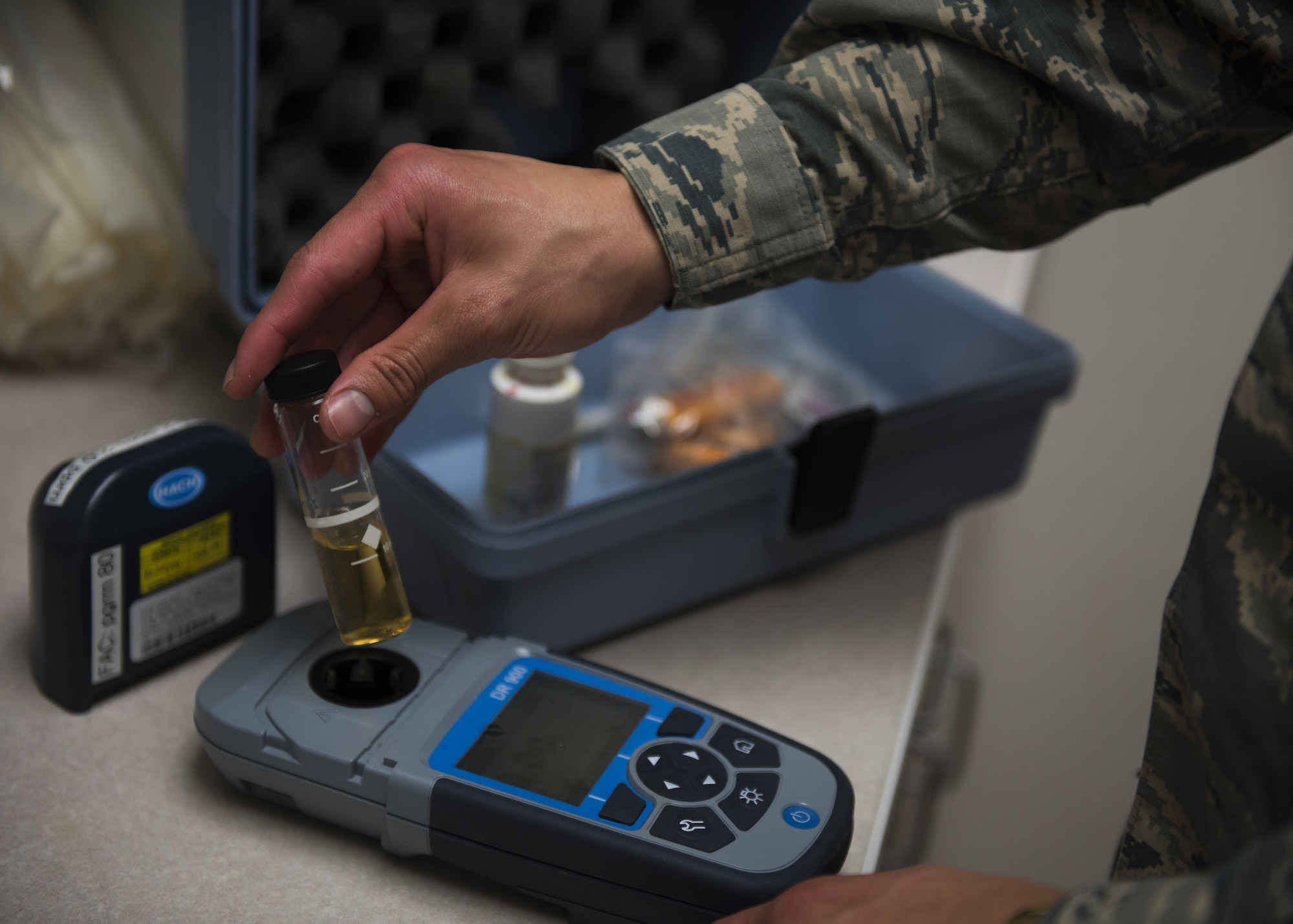 A hand holding a vial of water over a colorimeter.