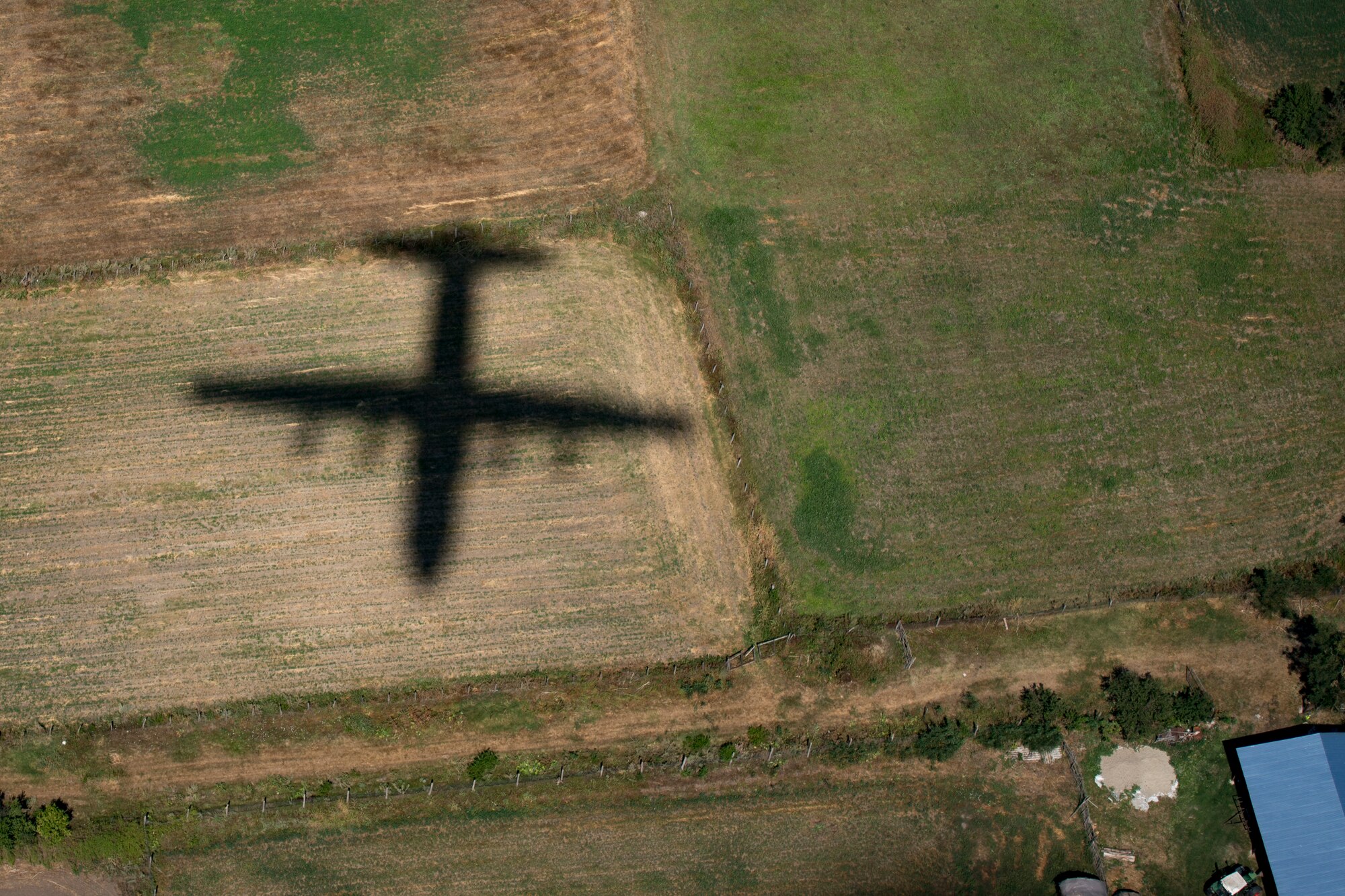 A U.S. Air Force C-130J Super Hercules aircraft assigned to the 37th Airlift Squadron, Ramstein Air Base, Germany, casts a shadow as it flies over farmland in Romania during exercise Carpathian Summer 2018, Aug. 21, 2018. The 37th AS Airmen simulated a cargo drop to practice for the following day’s actual airdrop. (U.S. Air Force photo by Senior Airman Devin Boyer)