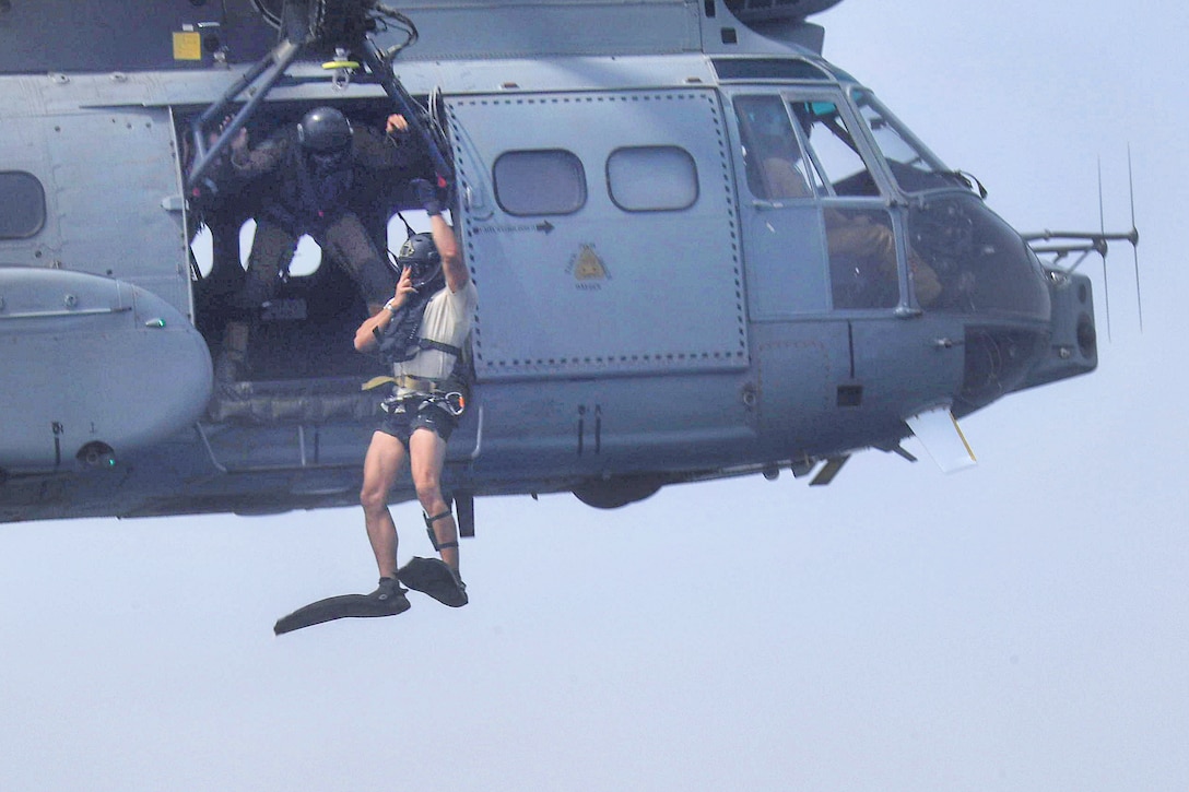A U.S. Air Force crew chief watches as an airman jumps out of a French SA 330 Puma helicopter.
