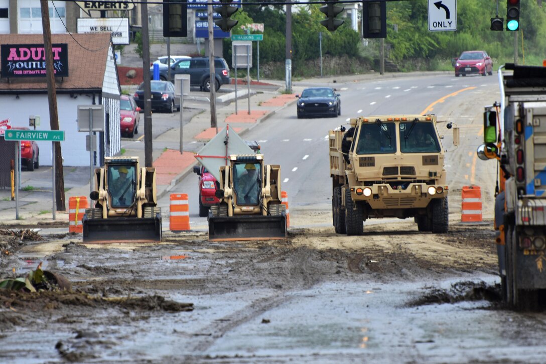 Soldiers operate skid-steer loaders to clear mud and debris from streets and parking lots.