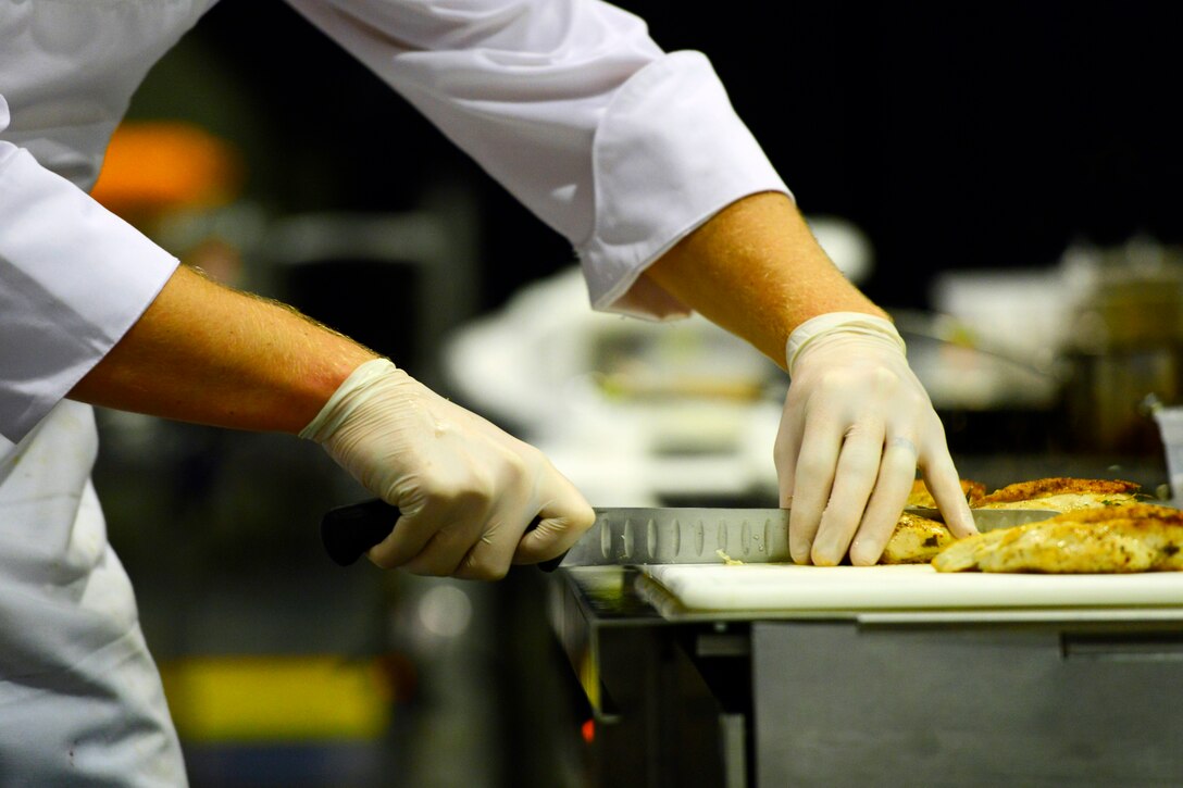 A Coast Guard member is shown cutting chicken during the American Culinary Federation Student Team Championships.