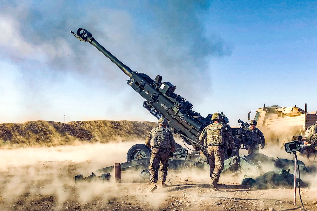 Soldiers approach a Howitzer after it is fired in the desert.