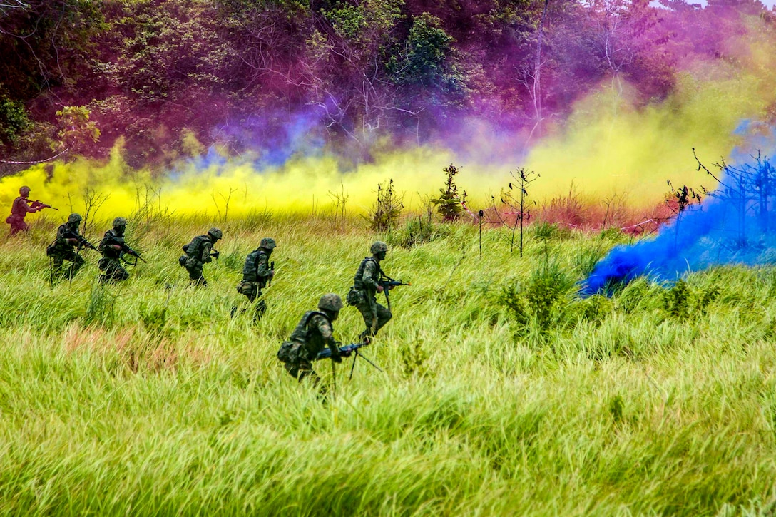 Soldiers advance through a field under cover of smoke.