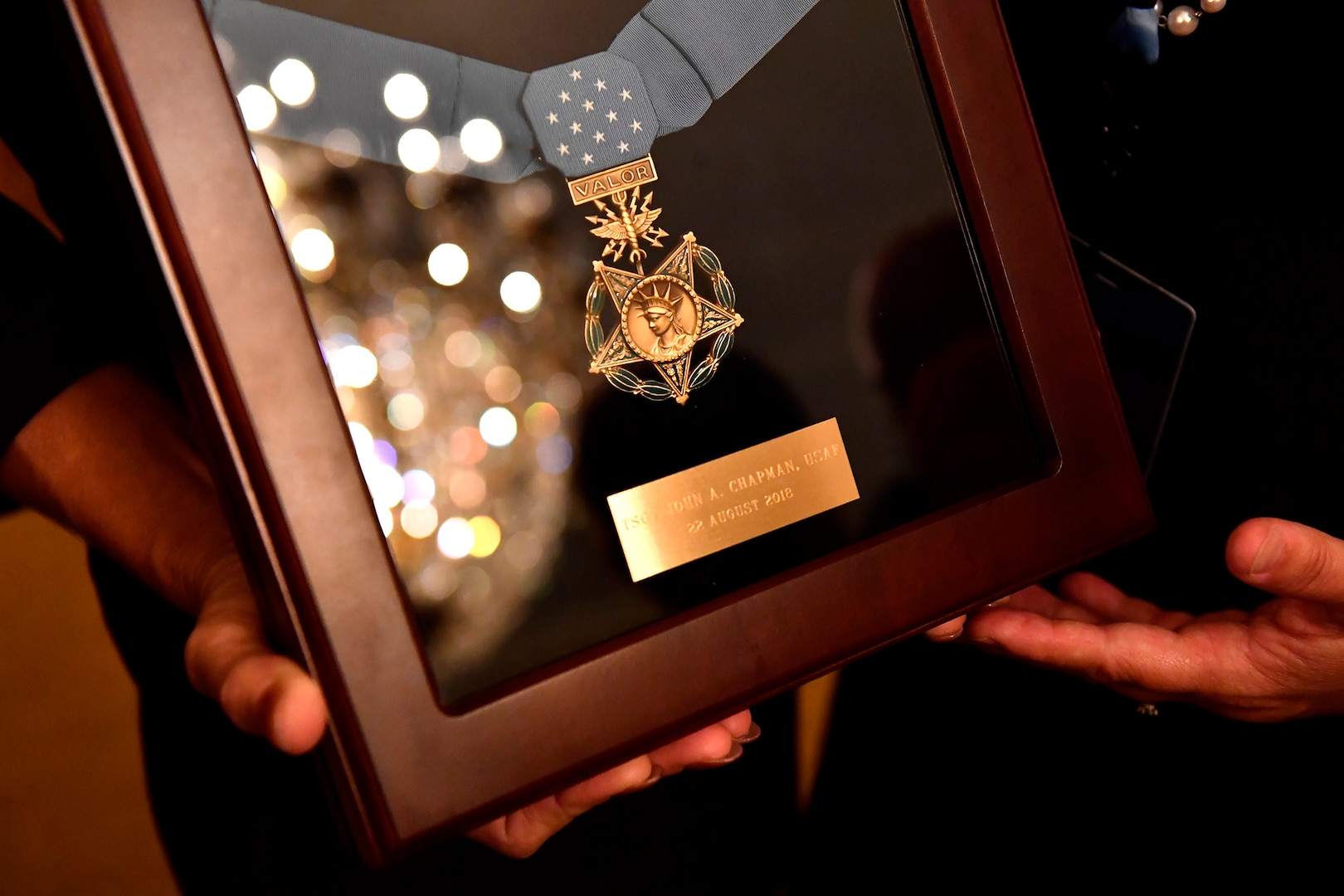 Valerie Nessel, the spouse of U.S. Air Force Tech. Sgt. John Chapman, holds up the Medal of Honor after receiving it from President Donald J. Trump during a ceremony at the White House in Washington, D.C., Aug. 22, 2018. Chapman was posthumously awarded the Medal of Honor for actions on Takur Ghar mountain in Afghanistan on March 4, 2002. His elite special operations team was ambushed by the enemy and came under heavy fire from multiple directions. Chapman immediately charged an enemy bunker through thigh-deep snow and killed all enemy occupants. Courageously moving from cover to assault a second machine gun bunker, he was injured by enemy fire. Despite severe wounds, he fought relentlessly, sustaining a violent engagement with multiple enemy personnel before making the ultimate sacrifice. With his last actions, he saved the lives of his teammates. (U.S. Air Force photo by Staff Sgt. Rusty Frank)