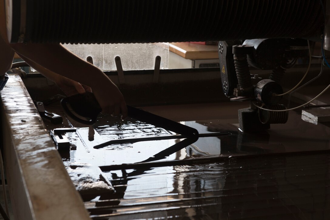 U.S. Air Force Airman 1st Class Thomas Kelley, 18th Equipment Maintenance Squadron metals technology journeyman, removes a newly cut part from a water-jet cutting machine Aug. 20, 2018, at Kadena Air Base, Japan. The 18th EMS is working to innovate their shop by training on the use of 3-D printers. When the training is complete, they will be able to create countless parts that are currently ordered, saving Kadena AB man-hours and the Air Force money.
