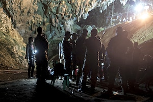 People stand silhouetted against light in a cave.