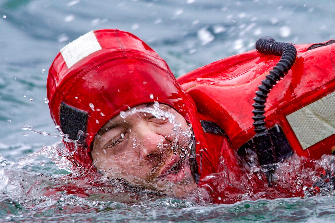 A coast guardsman swims wearing a full body suit.