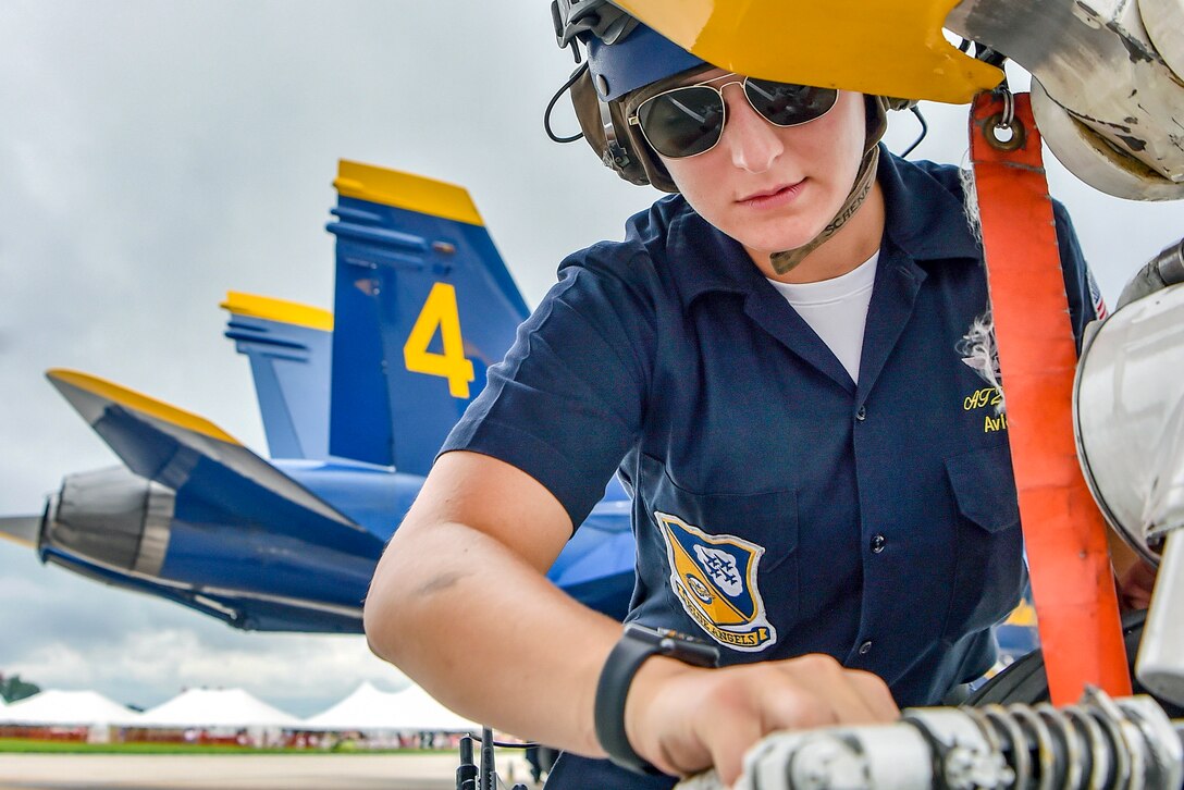 A naval officer cleans aircraft landing gear hardware.