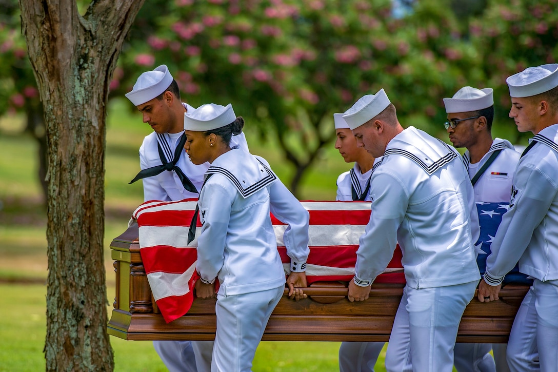 Sailors carry a coffin through a cemetery.