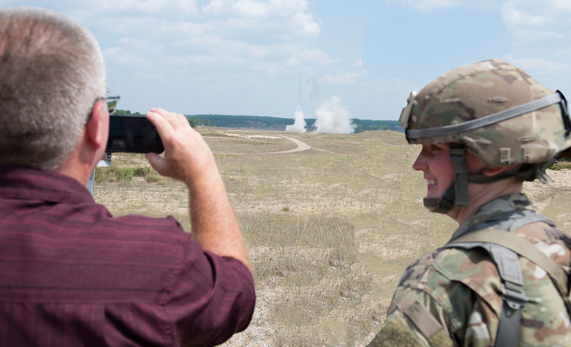 Spc. Heather M. Cote, a supply specialist assigned to the 197th Field Artillery Brigade, N.H. Army National Guard, smiles as her civilian employer, John Mercier records a HIMARS rocket launch demonstration on Aug. 14, 2018 at Camp Grayling, Mich. Mercier, and othe employers, visited their citizen-soldier employees during their annual training event as part of a tour with the N.H. Employer Support of the Guard and Reserve. (Photo by Staff Sgt. Kayla White, 157th Air Refueling Wing Public Affairs)
