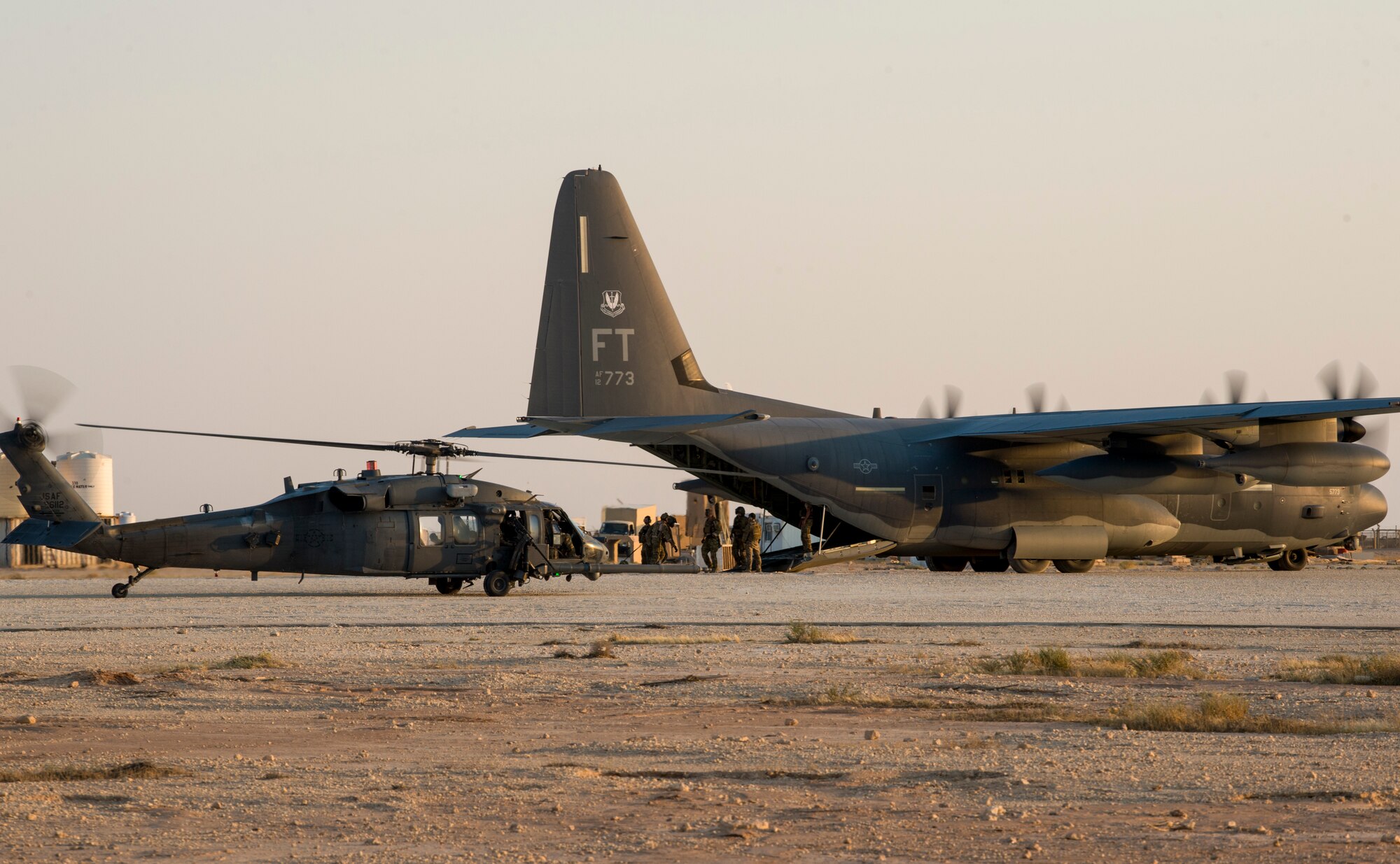 An HH-60G Pave Hawk provides security for an HC-130J Super Hercules assigned to the 26th Rescue Squadron while simulated survivors are loaded after a training scenario during a combat search and rescue exercise in Iraq, July 15, 2018. The HC-130J replaced HC-130P/Ns as the only dedicated fixed-wing personnel recovery platform in the Air Force inventory. Its mission is to rapidly deploy to execute combatant commander directed recovery operations to austere airfields and denied territory for expeditionary, all weather personnel recovery operations to include airdrop, air-land, helicopter air-to-air refueling, and forward area ground refueling missions. Battlefield Airmen assigned throughout the combined joint operational area conduct operations in support of Combined Joint Task Force - Operation Inherent Resolve. CJTF- OIR aims to enable and equip local forces to take ISIS head on while leveraging Coalition nation airpower to defeat ISIS in Iraq and Syria. (U.S. Air Force photo by SSgt Keith James)