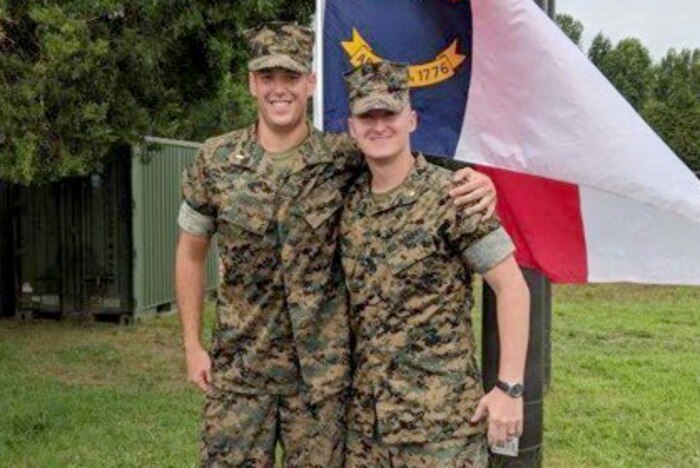 Two marines stand next to each other in front of a flag.
