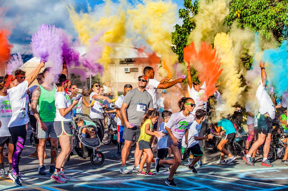 A crowd of people throw colorful powder into the air at a race starting line.