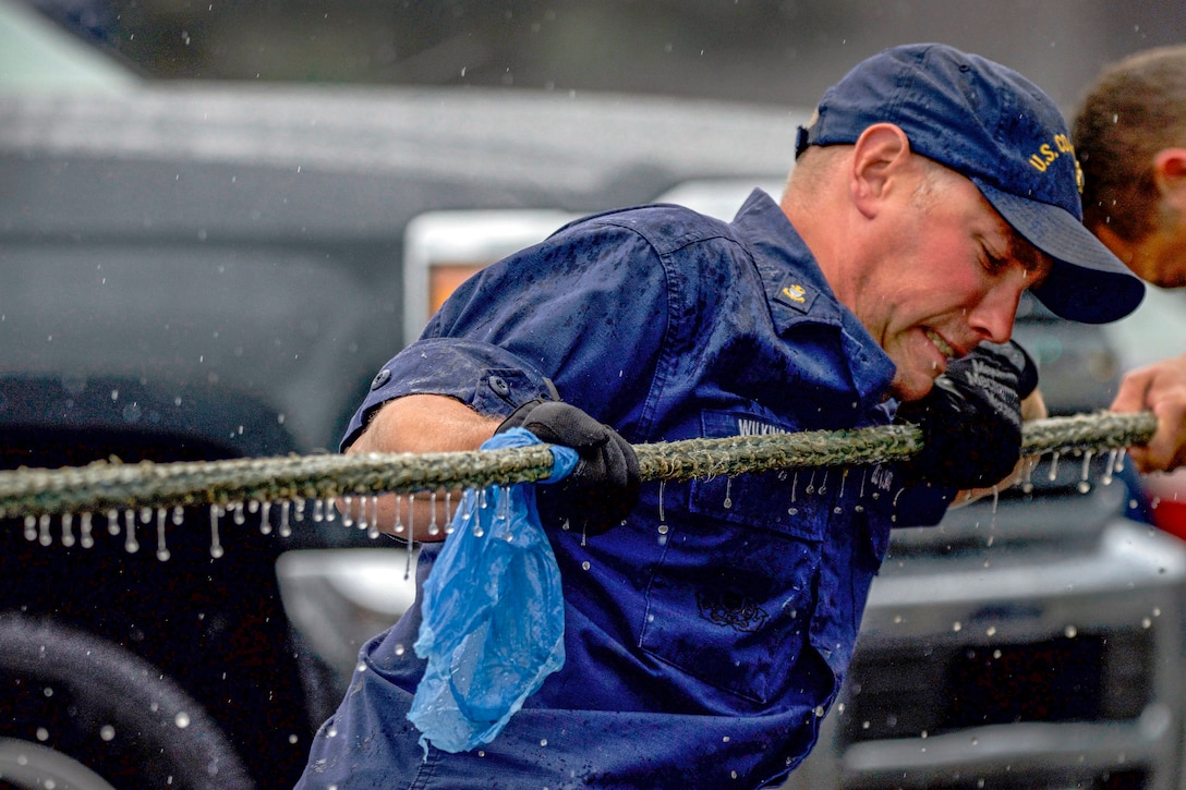 A coast guardsman pulls a wet rope.