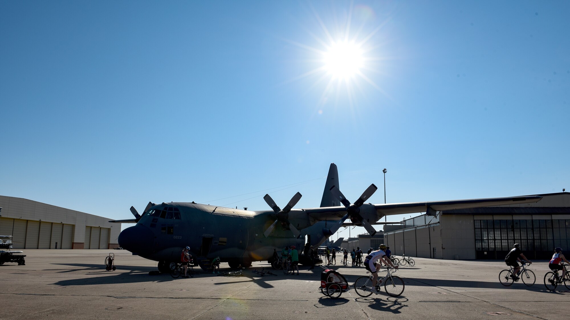 The sun shines over a C-130 as Hotter'N Hell riders pass by and stop to take pictures