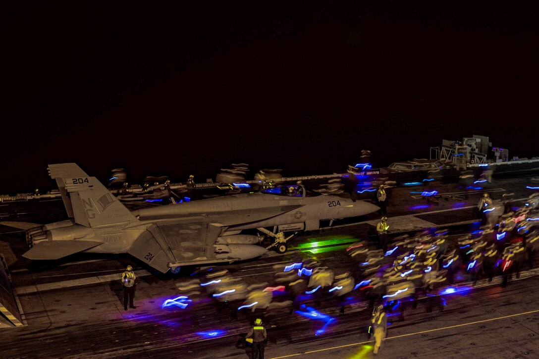 Sailors look for foreign objects or debris near an aircraft.