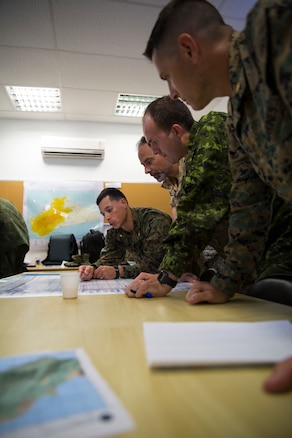 Military members from multiple countries talk at a table.