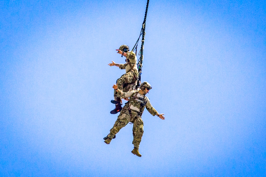 Two airmen hang from a rope attached to their uniforms.