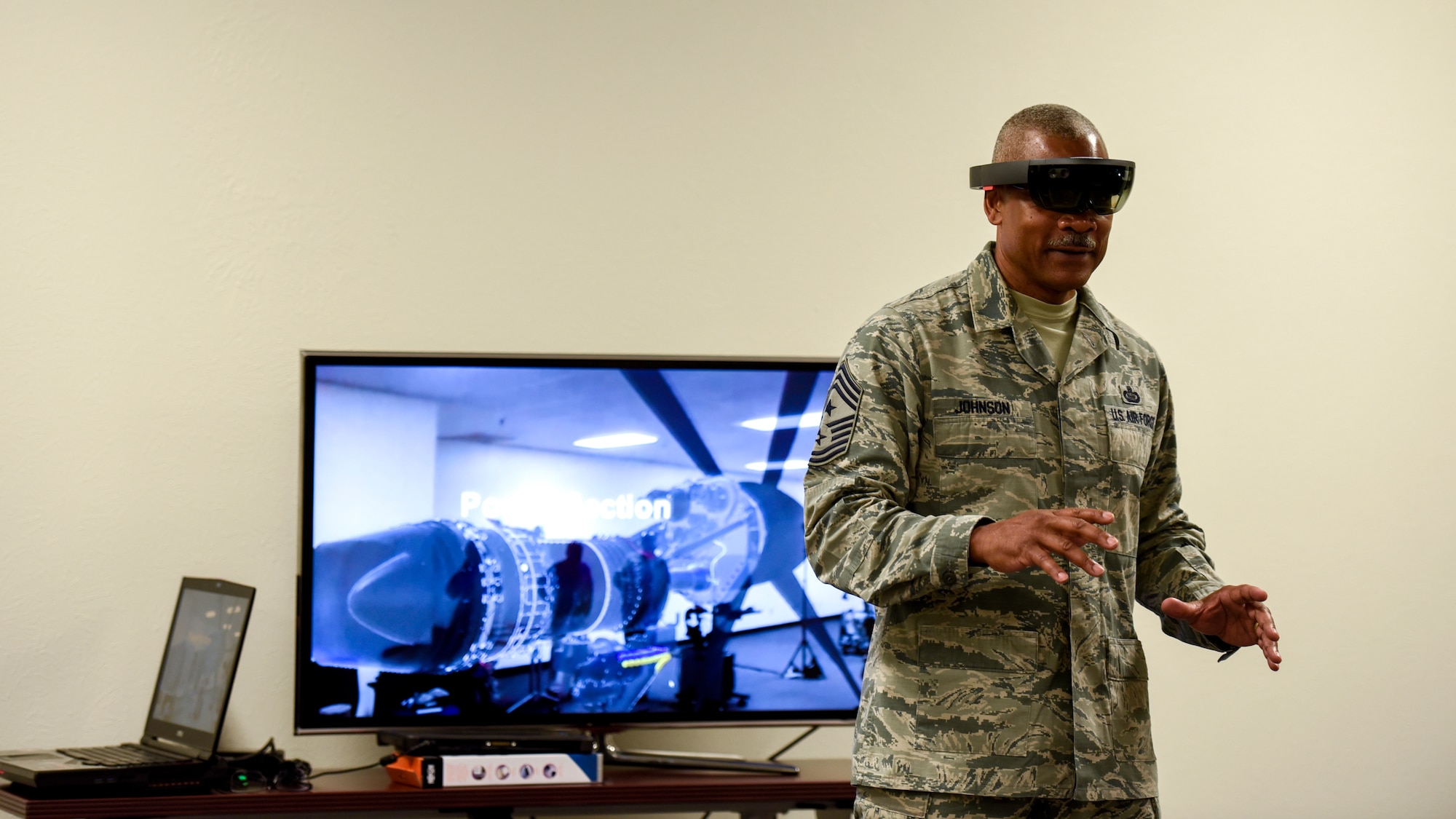 CMSgt. Jack Johnson Jr. walks around with futuristic glasses while a tv behind him shows what he sees.