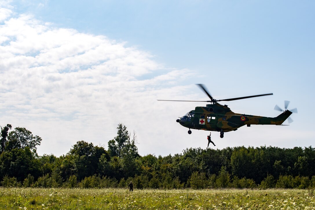 Romanian air force personnel hoist one of their own into an IAR-330 Puma helicopter after simulating a rescue mission with U.S. Air Force 37th Airlift Squadron pilots during a Survival, Evasion, Rescue, and Escape scenario in Bolovani, Romania, Aug. 24, 2018.