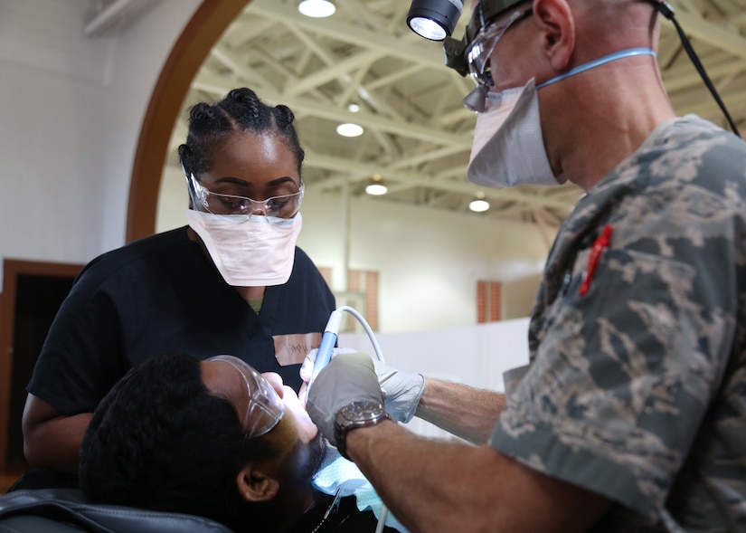 A Navy dental technician and an Air Force dentist work on a child's teeth.