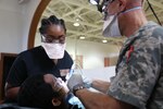 A Navy dental technician and an Air Force dentist work on a child