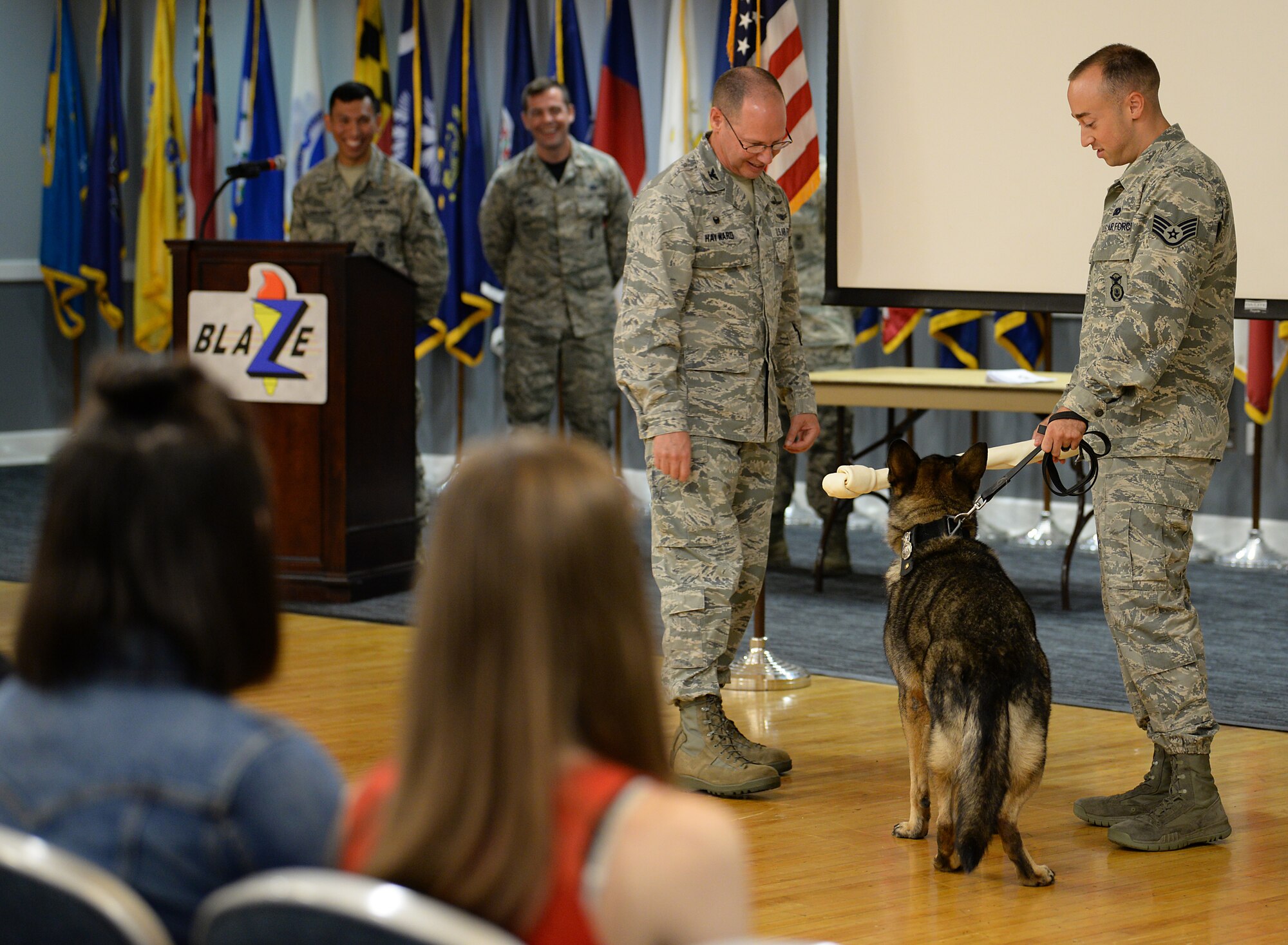 Col. Gary Hayward, 14th Mission Support Group commander, presents Military Working Dog Cherry, 14th Security Forces Squadron, a gift during her retirement ceremony Aug. 24, 2018, on Columbus Air Force Base, Mississippi, while her handler, Staff Sgt. Nicholas Heckler, former 14th SFS MWD handler, looks on. Cherry was assigned to the 14th Security Forces Squadron, faithfully serving 10 years in the U.S. Air Force. (U.S. Air Force photo by Airman Hannah Bean)