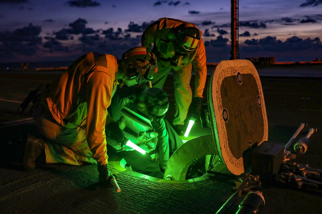 Sailors work behind a panel on the flight deck of a ship.
