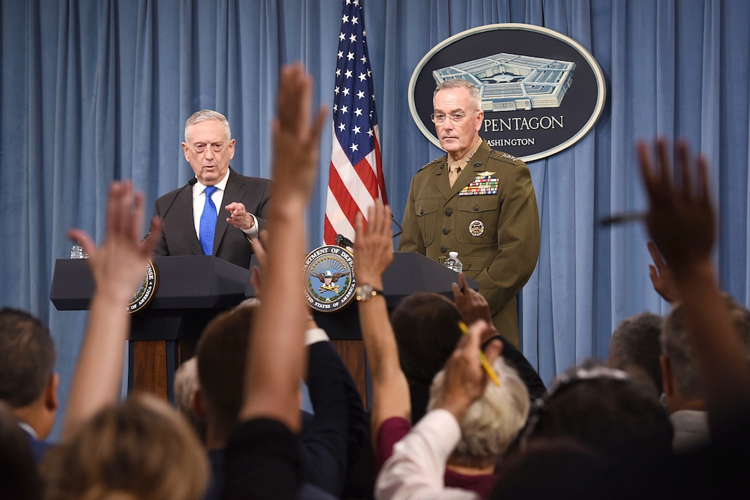 Defense Secretary James N. Mattis and Marine Corps Gen. Joe Dunford stand at lecterns facing reporters raising their hands.
