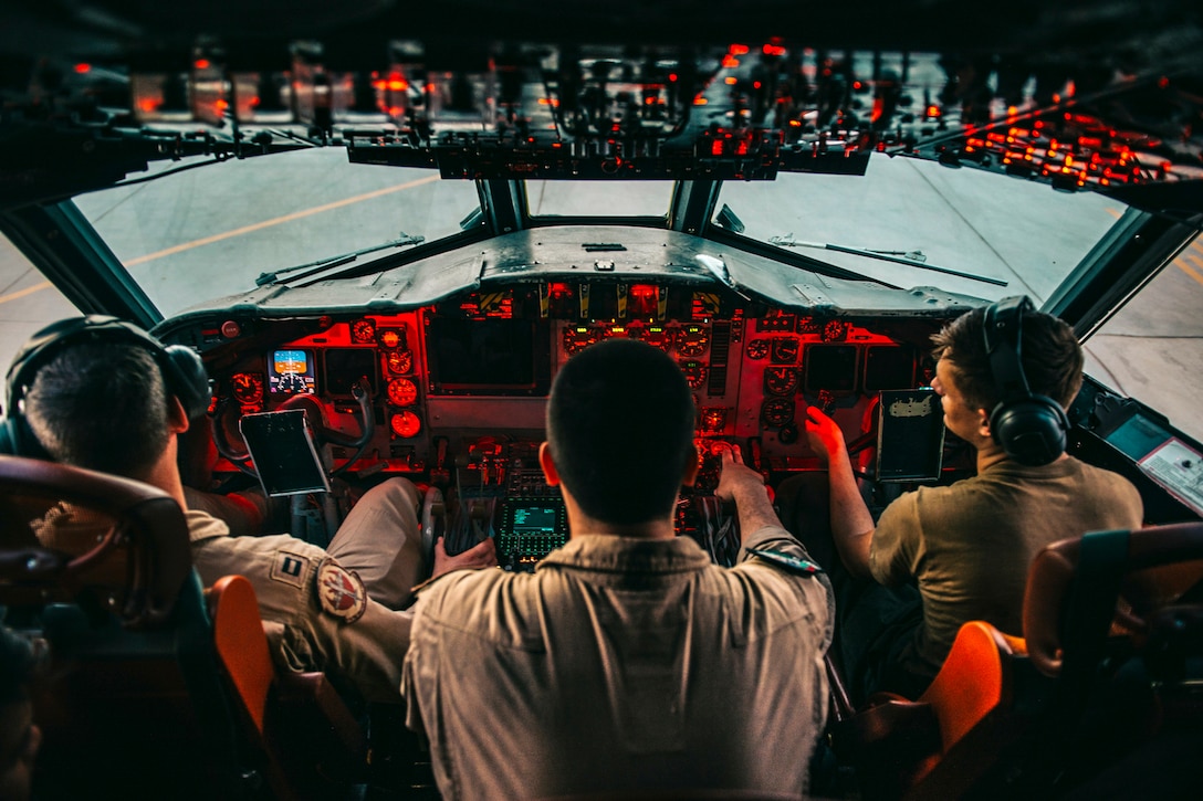 Three sailors, shown from behind, sit in a red-lit cockpit.