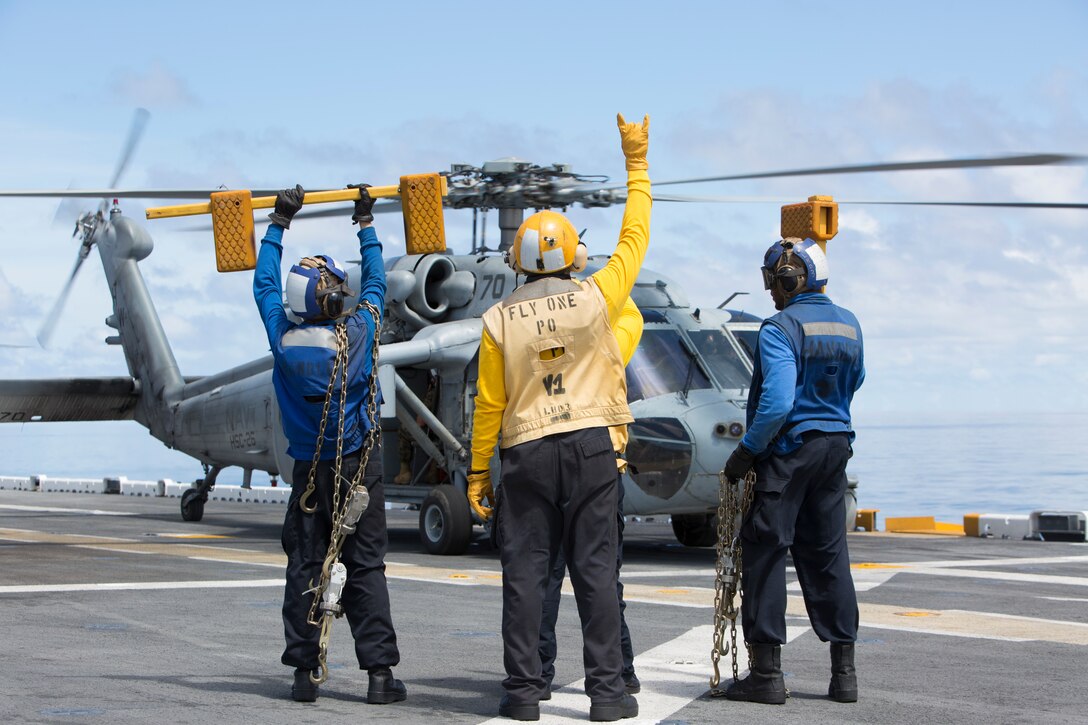 Navy Sailors signal the pilot prior to take off as Lt. Gen. Robert F. Hedelund, II Marine Expeditionary Force commanding general, and Vice Adm. Andrew Lewis, commander U.S. 2nd Fleet, depart to observe a visit, board, search and seizure evolution conducted by the 22nd Marine Expeditionary Unit at sea, Aug. 27, 2018. Hedelund and Lewis discussed how combining the capabilities of II MEF and the 2nd Fleet will strengthen joint-force partnership in the region and abroad. (U.S. Marine Corps photo by Pfc. Nicholas Guevara)