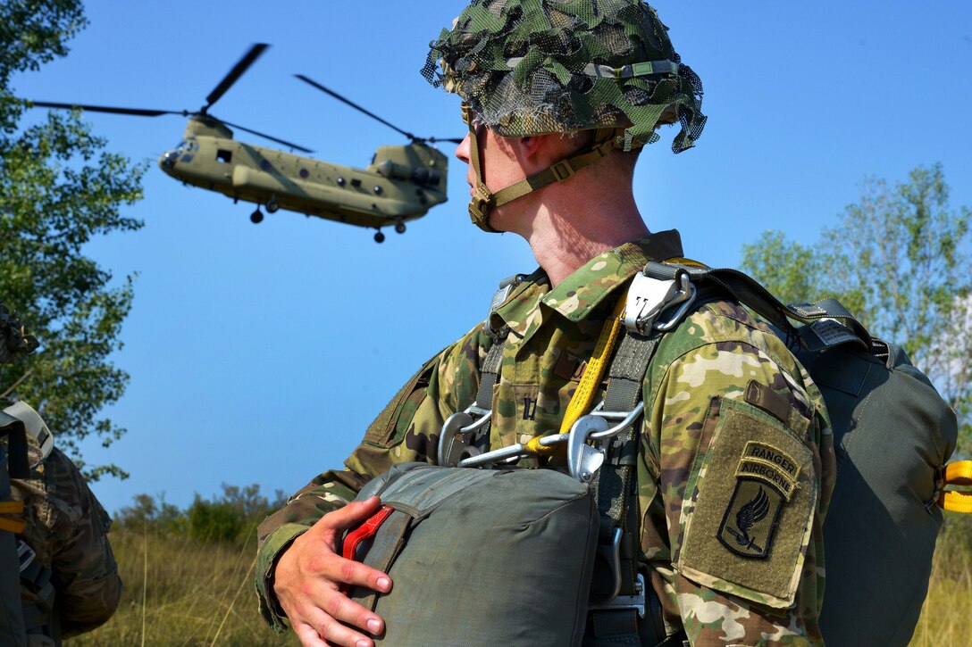 A U.S. paratrooper observes an approaching CH-47 Chinook helicopter landing before conducting airborne operations.