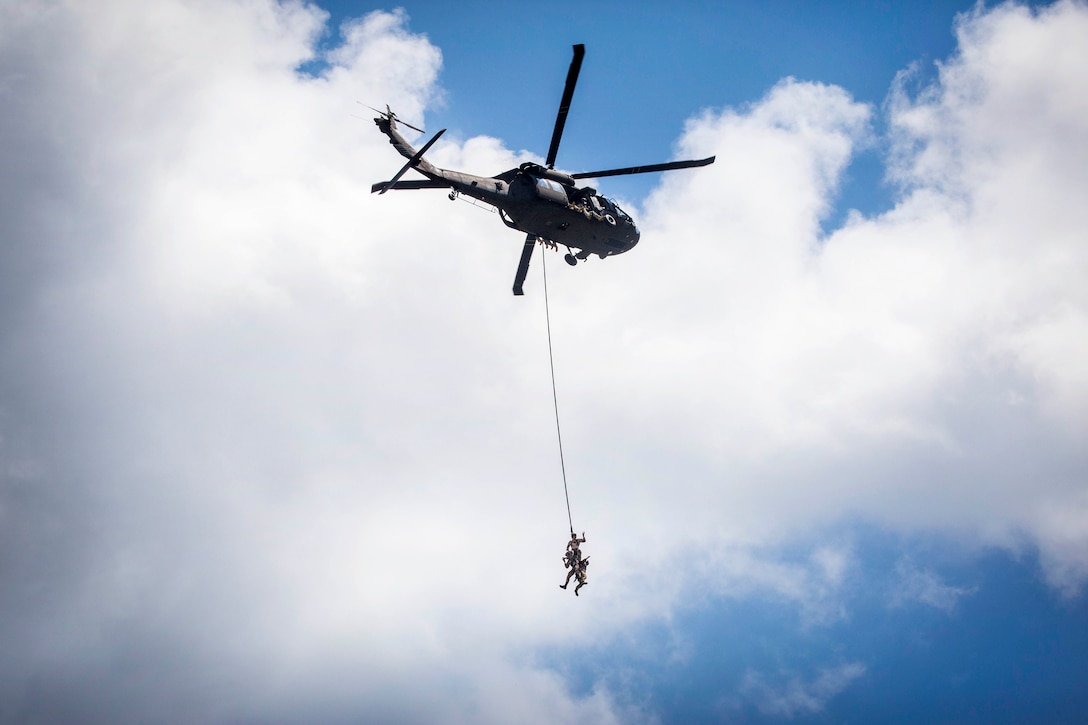 Airmen demonstrate a special extraction system as they hang from a UH-60L Black Hawk helicopter.
