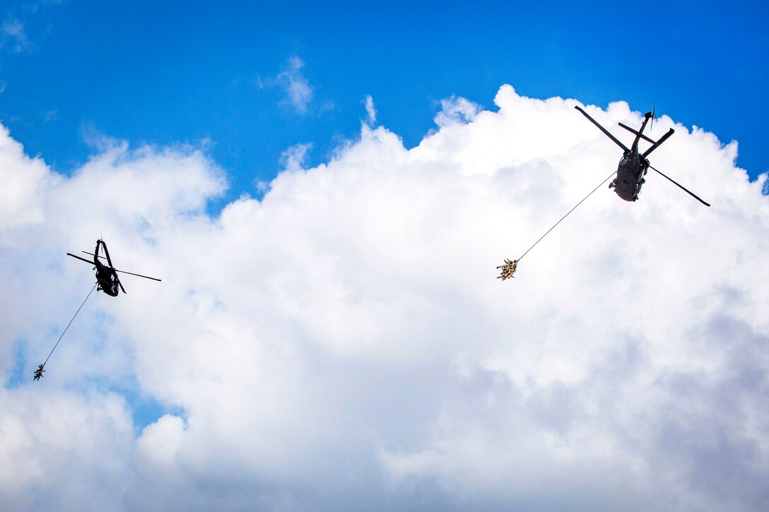 Airmen demonstrate a special extraction system as they hang from two UH-60L Black Hawk helicopters.