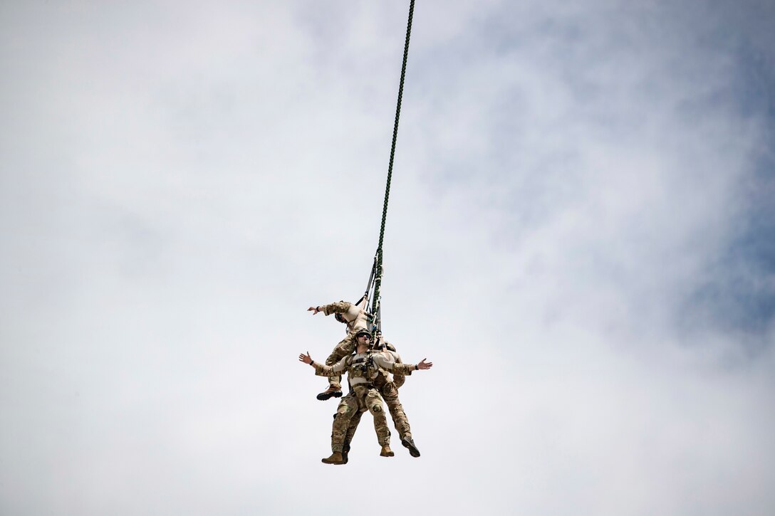 Airmen hang underneath a helicopter during a special extraction system demonstration.